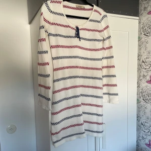 Randig stickad klänning från Jennifer - Vit stickad klänning med röda och marinblå ränder från Jennifer. Den typiska pippi-klånningen är långärmad och har en söt snörning vid halsringningen. Perfekt för Astrid Lindgrens värld i sommar!!