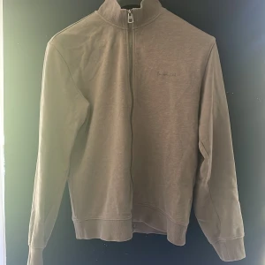 Beige ziptröja från Bondelid - Säljer en stilren beige ziptröja från Bondelid med hög krage och diskret broderad logga på bröstet. Tröjan har långa ärmar, ribbade muddar och är tillverkad i mjuk bomull. Perfekt för lager-på-lager och enkel att matcha med det mesta. Nypris 700:-