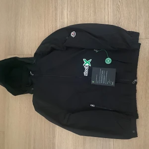 Svart vindjacka från Moncler - Svart vindjacka från Moncler med huva och hel dragkedja framtill. Jackan har klassisk Moncler-logga på ärmen och stilren design. Materialet är lätt och passar perfekt för blåsiga dagar. Snygg och enkel att matcha med streetwear eller casual outfits.