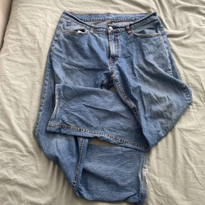 Blå jeans från Jacksonville, w36 l34 - Klassiska blå jeans från Jacksonville med raka ben och normal passform. Jeansen har fyra fickor, orange kontrastsömmar på baksidan och en snygg läderpatch bak i midjan. Tillverkade i slitstarkt denimtyg, perfekta för en avslappnad stil.