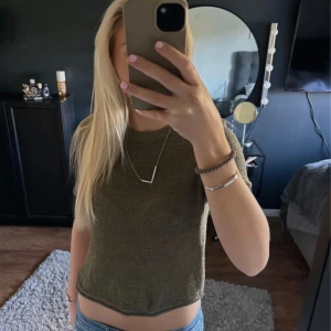 Olivgrön stickad topp - Säljer en olivgrön stickad topp med korta ärmar och rund hals. Toppen har en enkel och clean design, perfekt att matcha med jeans eller kjol. Den är croppad och har en mjuk känsla mot huden.