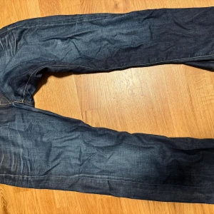 Replay Waitom jeans mörkblå - Snygga mörkblå Replay Waitom jeans med klassisk femficksdesign och coola detaljer på bakfickorna. Jeansen har kontrastsömmar och en stilren knapp framtill. Perfekta för dig som gillar en tidlös jeanslook. Står storlek 31/32, men passar mer som en 32-31/30