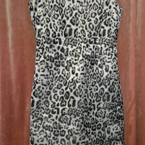 Leopardmönstrad kortklänning BB Studio - Snygg kort klänning från BB Studio med leopardmönster i svart och beige. Klänningen är ärmlös och har en figurnära passform. Materialet har en lätt glansig finish som ger en cool look. Perfekt för dig som vill sticka ut med ett djurmönster.
