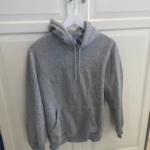 Grå hoodie från H&M Divided XS - En klassisk grå hoodie från H&M Divided i storlek XS. Tröjan har huva med snörning, stor känguruficka framtill och ribbade muddar vid ärmslut och nederkant. Perfekt för chill dagar eller när du vill ha en enkel och stilren look.