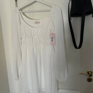 Vit klänning - Har lănga ärmar, lätt struktur i tyget och markerad midja som ger en enkel men elegant form. Passar perfekt till student, midsommar eller sommartest. Storlek S (36). Helt ny och aldrig använd och prislappen sitter kvar. Jag bestallde flera klanningar infor studenten och beholl en annan - den har blev over. Ordinarie pris: 399 kr.
