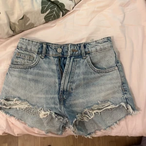 Ljusblå jeansshorts med fransar från Zara - Säljer ett par ljusblå jeansshorts med råa franskantade benslut och klassisk femficksdesign. Shortsen har medelhög midja!