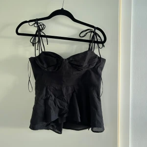 Svart linnetopp med volang och knytband - Säljer en svart linnetopp med volangdetalj och knytbara axelband från Zara i storlek M. Aldrig använd