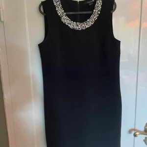 Audrey Hepburn klänning - Snygg svart ärmlös klänning från Forever 21 med dekorativa pärlor runt halsringningen. Klänningen har en klassisk, rak passform och är tillverkad i polyester med dragkedja i ryggen. Perfekt för dig som vill sticka ut med eleganta detaljer.