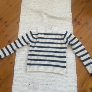 Vit och marinblå randig stickad tröja från H&M - Säljer en stickad tröja från H&M i vitt med marinblåa horisontella ränder. Tröjan har rund halsringning, långa ärmar och ribbade muddar. Perfekt för en avslappnad och stilren look.