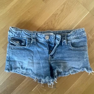 Lågmidjade jeansshorts i stl 146 från Gina Young - Säljer ett par blå jeansshorts från Gina Tricot Young i stl 146. Shortsen har låg midja samt bakfickor med knapp. I använt men fint skick.
