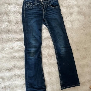 Mörkblå jeans från Gina Tricot - Säljer ett par mörkblå jeans från Gina Tricot i klassisk modell med vita kontrastsömmar och fem fickor. Jeansen har normal passform och raka ben, samt knapp och dragkedja framtill.