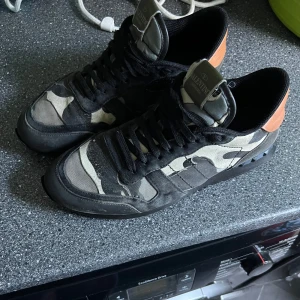 Valentino Rockrunner sneakers med camouflage - Säljer ett par Valentino Rockrunner sneakers med svart och grått camouflage-mönster. Skorna är i relativt bra skick efter ha varit med nått år (tyvärr ingår ingen box därmed priset)
