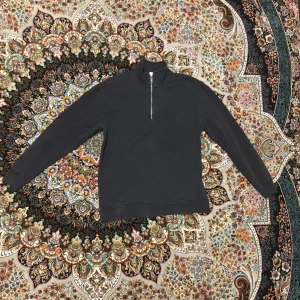 Svart tröja med halv dragkedja från DeFacto - Säljer en svart långärmad tröja från DeFacto med hög krage och halv dragkedja framtill. Perfekt för en stilren och enkel look. Tröjan är i mjukt material och passar till många tillfällen.