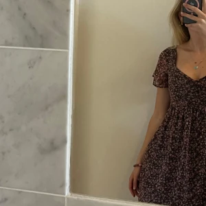 Blommig kortklänning med v-ringning - Söt kortklänning med svart botten och små rosa blommor. Från Hollister, aldrig använt och har prislappen kvar! Klänningen har v-ringning, korta ärmar och en lätt utställd kjol. 