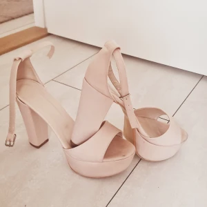 Beiga platåklackar med öppen tå - Säljer ett par snygga beiga platåklackar med bred klack och öppen tå. Skorna har en justerbar rem runt vristen och är perfekta för dig som vill ha extra höjd och stil. Passar till många olika outfits!