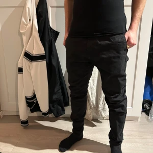 Svarta chinos - Säljer ett par svarta chinos från Jack & Jones med normal passform och raka ben. Byxorna har klassisk design med fickor på sidorna och baktill. Perfekta för en stilren och enkel look.