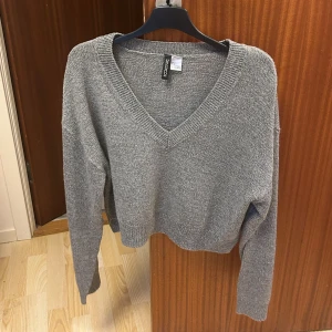 Grå stickad v-ringad tröja från H&M - Säljer en grå stickad tröja från H&M med v-ringning och långa ärmar. Tröjan har en avslappnad passform och är perfekt för kyligare dagar. Enkel och stilren design som passar till det mesta.