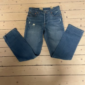 Levis 501 blå jeans - Klassiska blå Levis 501 jeans med raka ben och knappgylf. Jeansen har en vintage look med lätt slitna detaljer framtill och femficksdesign. Perfekta för en avslappnad och tidlös stil. Pris kan diskuteras vid snabb affär. 