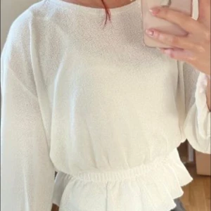 Vit blus med resår i midjan - Säljer en söt vit blus med rund halsringning och långa ärmar. Blusen har resår i midjan som ger en fin form och lätt volang nedtill. Perfekt att styla med jeans eller kjol.