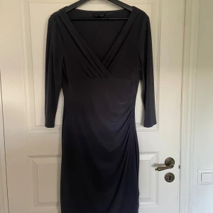 Mörkgrå/blå klänning från Ralph Lauren - Säljer en elegant mörkgrå/blå klänning från Ralph Lauren med v-ringning. Klänningen har draperad detalj i sidan och är tillverkad i ett mjukt, stretchigt material som ger en smickrande passform. Är i nyskick!!!! (Pris diskuteras)