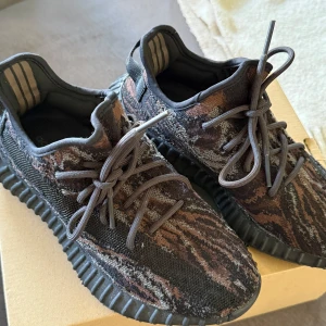 Adidas Yeezy Boost 350 V2 MX Rock - Säljer ett par Adidas Yeezy Boost 350 V2 i färgen MX Rock. Skorna har ett stickat mönster i svart, brunt och grått med svarta snören och en bekväm, ribbad sula. Perfekta för dig som gillar streetwear och vill sticka ut.