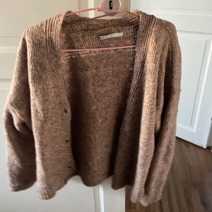 Brun stickad kofta från only  - Mysig brun stickad kofta från only med lång ärm och knappar framtill. Koftan har en avslappnad passform och är perfekt för lager-på-lager-stil. Passar till både jeans och klänning.