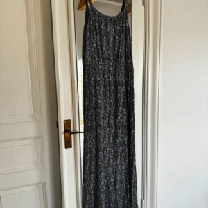 Blå blommig klänning - Lång, ärmlös klänning med smala ställbara axelband och ett blommigt mönster i blått och vitt. Fint skick! Färgen är mest rättvis på sista bilden.