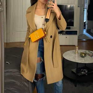 Beige kappa från Mango - Säljer en superfin beige kappa från Mango i mycket bra skick. Den har ett bälte i midjan och knappar framtill. Perfekt för höst och vår! Storleken är dam xs och den är långärmad. Passar både till vardags och lite finare tillfällen.