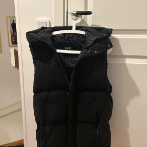 Svart väst från Zara med huva - Säljer en svart väst från Zara med huva och dragkedja framtill. Västen har två fickor med dragkedja och en hög krage. Perfekt för lager-på-lager och enkel att matcha. Inga defekter. Storlek S