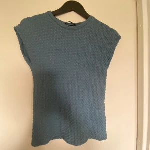 Blå strukturerad topp från Zara - Säljer en blå topp från Zara med strukturerat tyg och rund halsringning. Toppen är ärmlös och har en enkel, stilren design som passar perfekt till många olika outfits. Blåturkos färg!