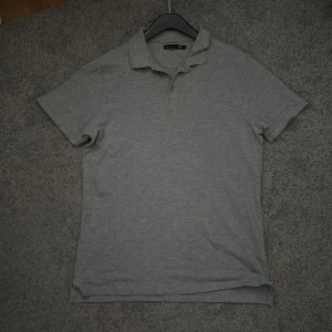 Grå pikétröja från 157 - Säljer en klassisk grå pikétröja från 157 i storlek L. Tröjan har korta ärmar, krage och knäppning framtill. Perfekt för en avslappnad och stilren look.