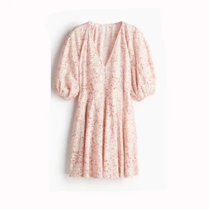 Ljusrosa blommig klänning med puffärmar - Supersöt ljusrosa klänning med blommigt mönster och v-ringning. Klänningen har puffiga korta ärmar och en luftig passform som ger en romantisk vibe. Perfekt för varma dagar och somriga tillfällen.