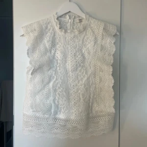 Vit spetsblus från ONLY - Superfin vit spetsblus med söta detaljer och mönstrad spets. Blusen är ärmlös och har en rund halsringning med vågiga kanter.