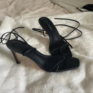 Svarta klackskor med snörning från Boohoo -  Stilrena svarta klackskor från Boohoo med tunna remmar och snörning runt vristen. perfekta för att lyfta din outfit. 