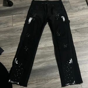 Gallery dept jeans - Säljer ett par svarta gallery dept flare jeans med ett stretchigt matrial. Byxorna har vita färgstänk och slitningar på flera ställen för en edgy look. Perfekta för dig som gillar streetstyle och vill sticka ut.