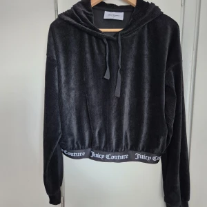 Svart hoodie från Juicy Couture - Säljer en svart hoodie från Juicy Couture med croppad passform och huva. Tröjan har långa ärmar och resår med logotypen Juicy Couture nedtill. Tillverkad i mjuk polyesterblandning med lite elastan för extra stretch. Det finns också shorts ( det är en set) som ingår i priset.