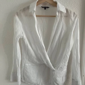 Vit omlottblus från Massimo Dutti - Säljer en stilren vit omlottblus från Massimo Dutti med krage och långa ärmar. Blusen har subtila ränder i tyget och en fin detalj i midjan för en snygg passform. Perfekt för dig som gillar klassisk och fräsch stil. Perfekt till sommaren och passar så bra till ett par jeans eller kjol.