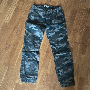 Levi's camo joggerbyxor med snörning - Camo-mönstrade joggerbyxor från Levi's med elastisk midja och snörning. Byxorna är tillverkade i 100% bomull och har muddar vid bensluten. Perfekta för en avslappnad och cool stil.