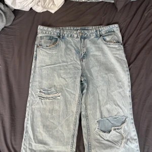 Ljusblå slitna jeans från H&M Divided - Ljusblå jeans med slitningar och hål på båda benen från H&M Divided. Modellen är rak och har klassiska fem fickor samt knapp- och dragkedjegylf. Perfekta för en avslappnad och trendig look.
