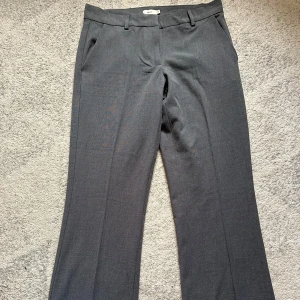 Mörkgrå bootcut  kostymbyxor - Snygga mörkgrå kostymbyxor från NELLY med raka ben och klassisk passform. Byxorna har hällor för bälte, sidofickor fram och fuskfickor bak. Perfekta för en clean och stilren look. Materialet känns mjukt och följsamt. Storlek 36 och true to size