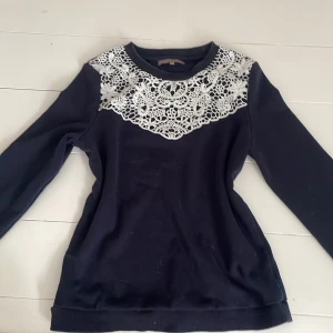 Mörkblå tröja med spets från Mint & Berry - Supersnygg mörkblå tröja från Mint & Berry i storlek S. Tröjan har långa ärmar och en unik vit spetsdetalj över axlar och bröst som ger en romantisk vibe.  Materialet känns mjukt och bekvämt.