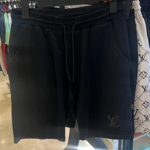 Svarta Louis Vuitton shorts med snörning - Finns alla storlekar!! Svarta shorts från Louis Vuitton med elastisk midja och snörning framtill. Klassisk LV-logga på ena benet och två sidofickor. Perfekta för en avslappnad och stilren look.