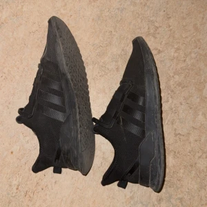 Svarta Adidas sneakers i mesh - Svarta Adidas sneakers med klassiska tre ränder på sidorna. Ovandelen är i ventilerande mesh och skon har en platt sula. Perfekta för en sportig look och funkar lika bra till jeans som till träningskläder.