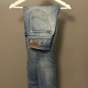 Lee Luke jeans blå W30 L32 - Snygga Lee Luke jeans i klassisk blå tvätt med slitningar och smal passform. Jeansen har fem fickor, dragkedjegylf och Lee-logga på bakfickan. Perfekta för dig som gillar en modern och stilren look.
