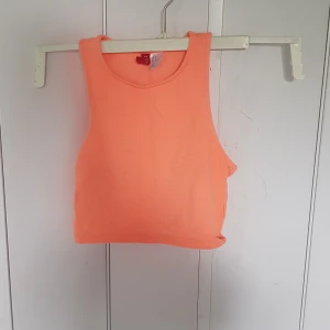 Neonorange linnetopp från H&M Divided - Säljer en neonorange linnetopp från H&M Divided. Toppen är croppad med breda axelband och rund halsringning. Perfekt för varma dagar och enkel att styla till jeans eller shorts. Materialet är mjukt och stretchigt för en bekväm känsla.