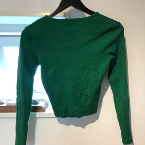 Grön långärmad tröja från Pigalle - Enkel och stilren grön långärmad tröja från Pigalle i storlek XS. Tröjan är ribbad och har en tight passform med rund halsringning. Perfekt att matcha med jeans eller kjol för en clean look.