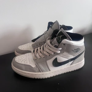 Nike Air Jordan 1 grå/vita sneakers - Säljer ett par Nike Air Jordan 1 sneakers i grått och vitt, svart. Nike-logga på sidorna och Air Jordan-märke vid ankeln. Ovandel i skinn och syntet, perfekt för dig som gillar streetstyle. Skick 10/10 hör av dig vid frågor.