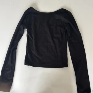 Svart långärmad topp öppen i ryggen - En svart, croppad långärmad topp som är lite öppen o ryggen. Tillverkad i mjukt bomullsmaterial för en bekväm känsla hela dagen. Endast använd fåtal gånger.