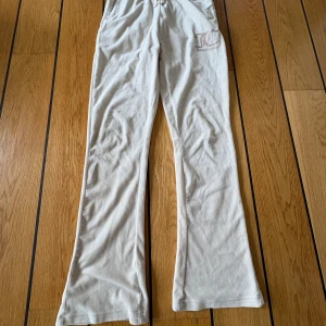 Beiga mjukisbyxor Juicy Couture - Supermysiga beiga mjukisbyxor från Juicy Couture med broderad logga framtill. Byxorna har dragsko i midjan, flare och bakfickor. Perfekta för chill dagar och har den klassiska Juicy-stilen.