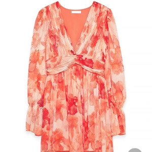 Blommig kortklänning med v-ringning - Superfin kortklänning med blommigt mönster i rött och rosa toner. Djup v-ringning, långa puffiga ärmar och markerad midja. Klänningen har plisserade detaljer och flowy material som känns lätt och somrigt.